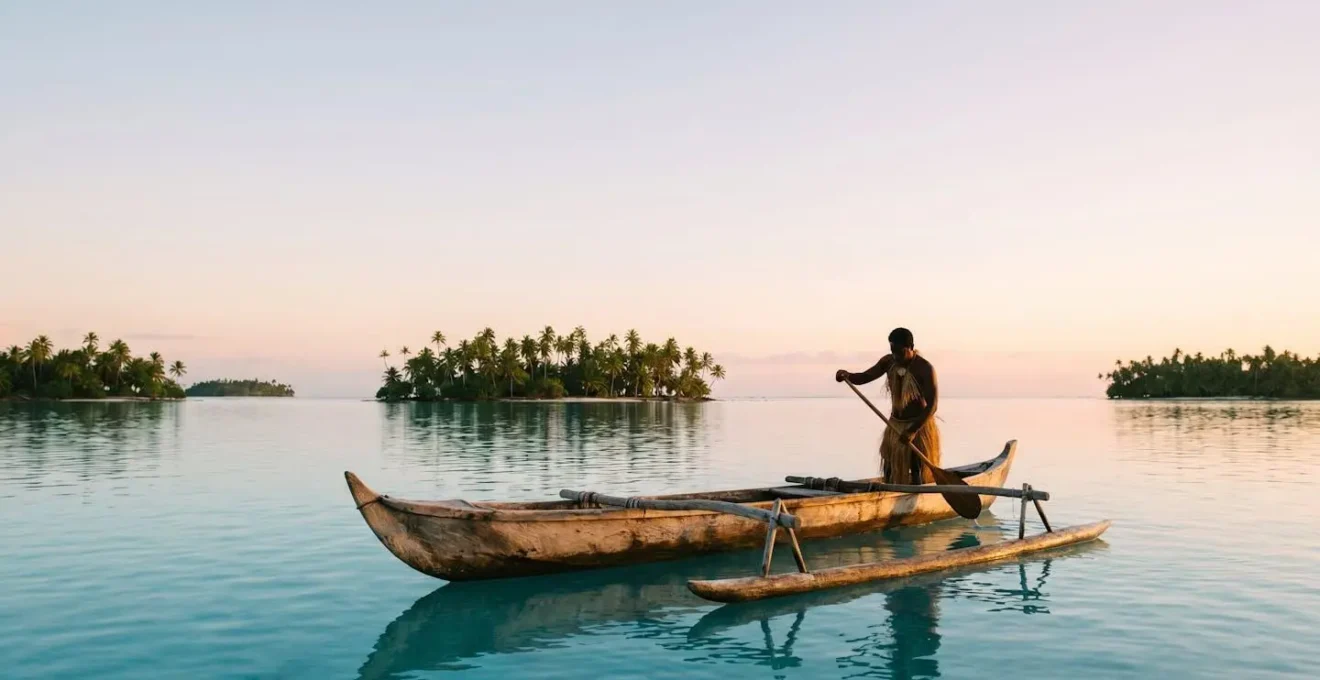 Pirogue polynesienne traditionnelle glissant seule sur un lagon turquoise a l'aube, loin des complexes hoteliers