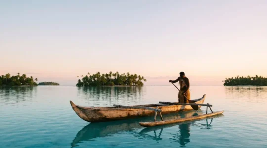 Pirogue polynesienne traditionnelle glissant seule sur un lagon turquoise a l'aube, loin des complexes hoteliers